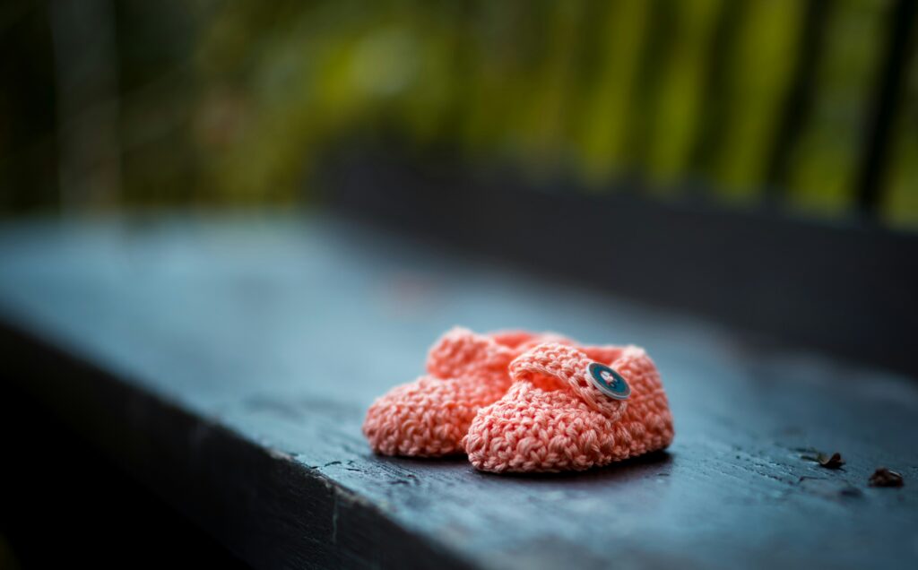 Cute pink baby booties on wooden bench, handcrafted with buttons, symbolising warmth, love, and new beginnings.