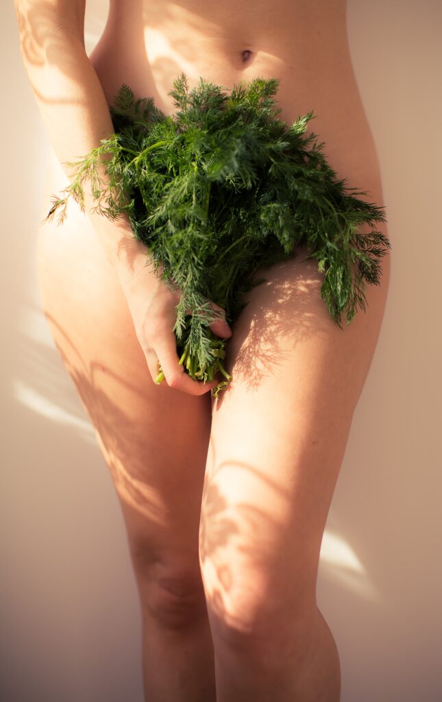 naked woman holding leaves in front of her pelvis