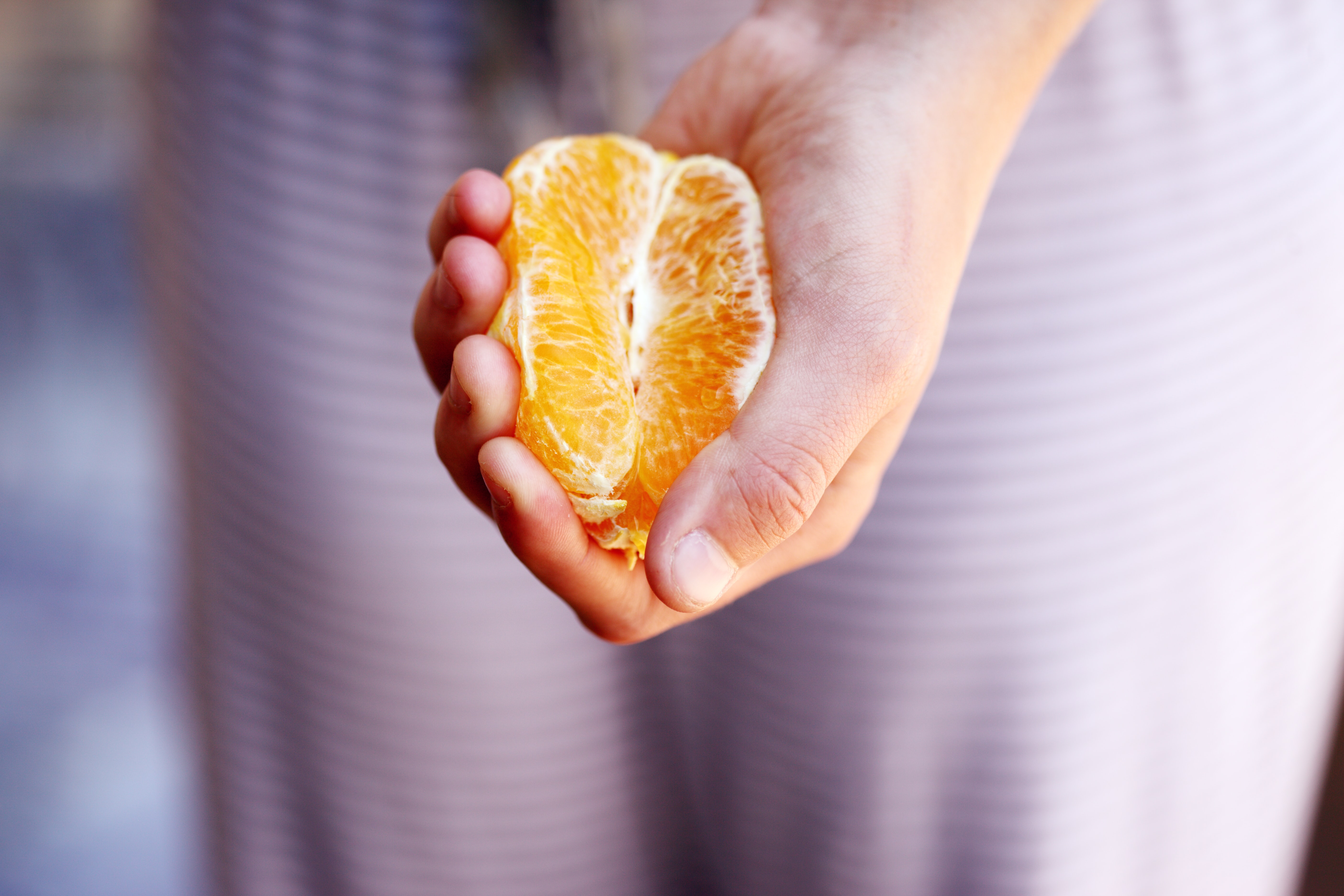 Hand holding a fresh orange slice, showcasing its vibrant colour and juicy texture against a blurred background.
