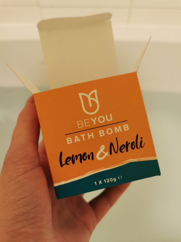 Hand holding an open BeYou Lemon & Neroli bath bomb box, enhancing bath time with refreshing citrus scent.