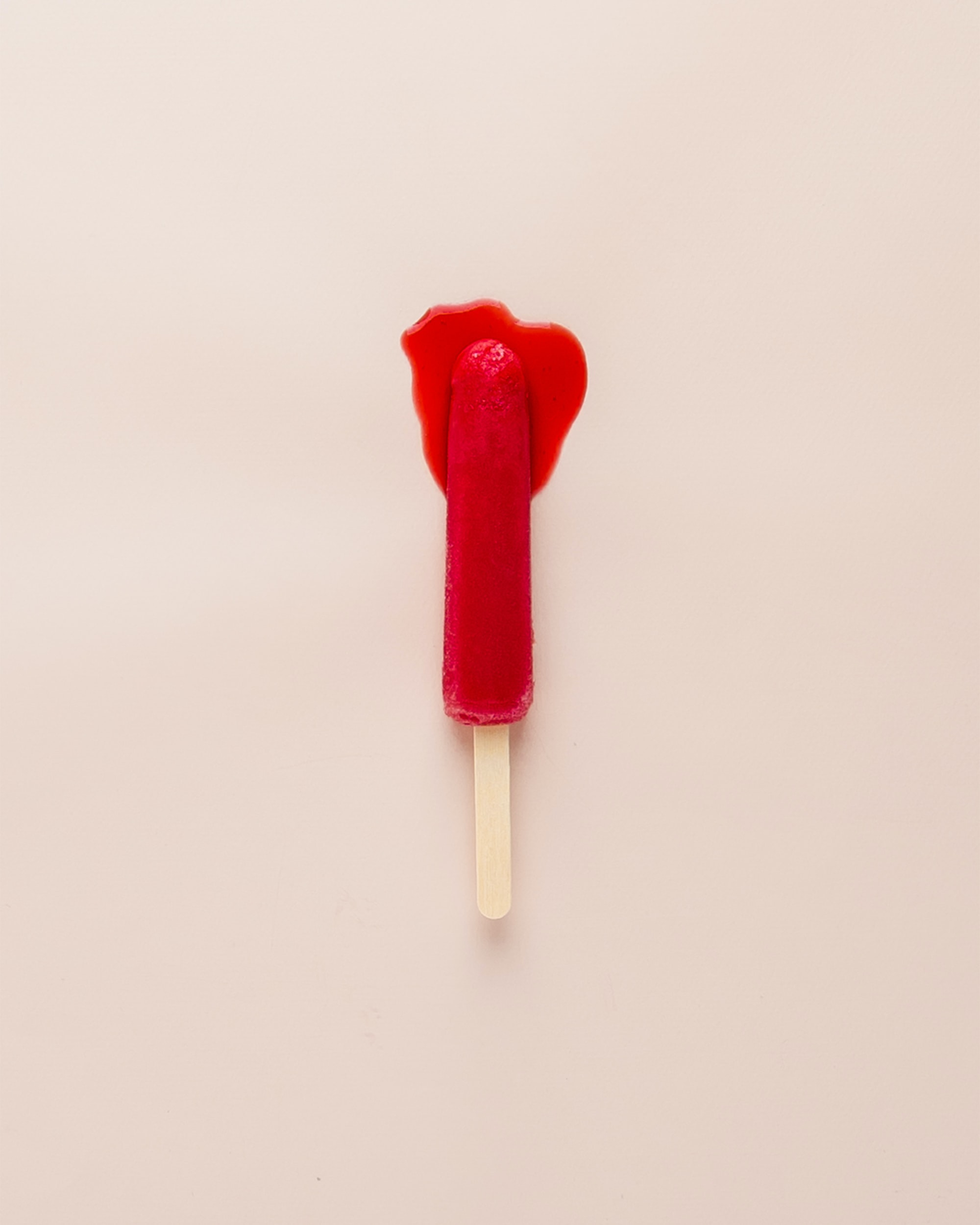 Red ice lolly melting on a light surface