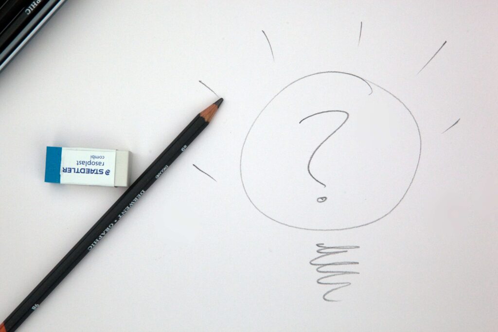 Pencil and eraser on paper with question mark sketch, symbolising creativity and brainstorming ideas.