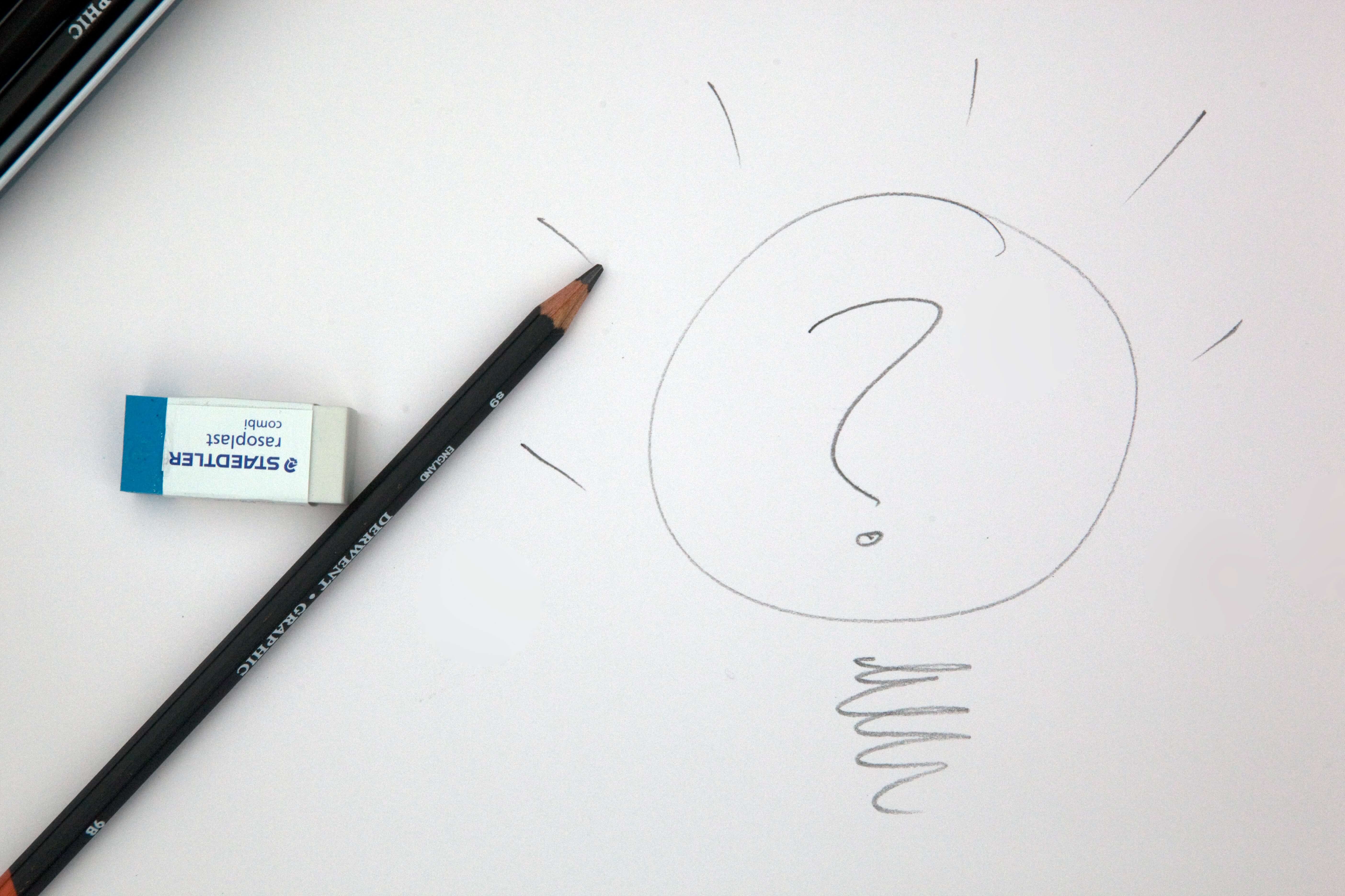 Pencil and eraser on paper with question mark sketch, symbolising creativity and brainstorming ideas.