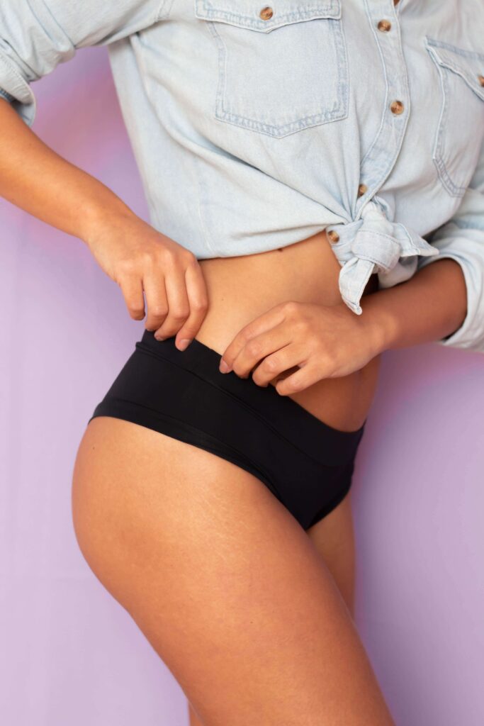 Woman in a tied denim shirt and black underwear against a lavender background. Fashion and style concept.