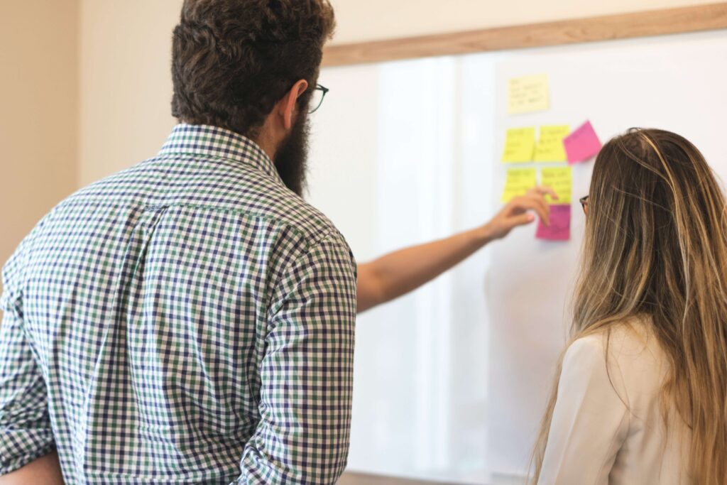 Two colleagues brainstorming with sticky notes on a whiteboard during a collaborative office meeting.