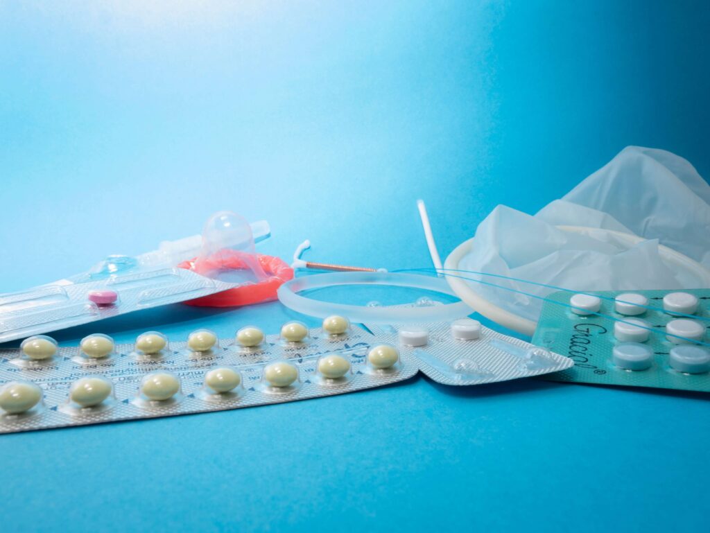 Various contraceptives on blue background, including pills and condoms, promoting safe sexual health.