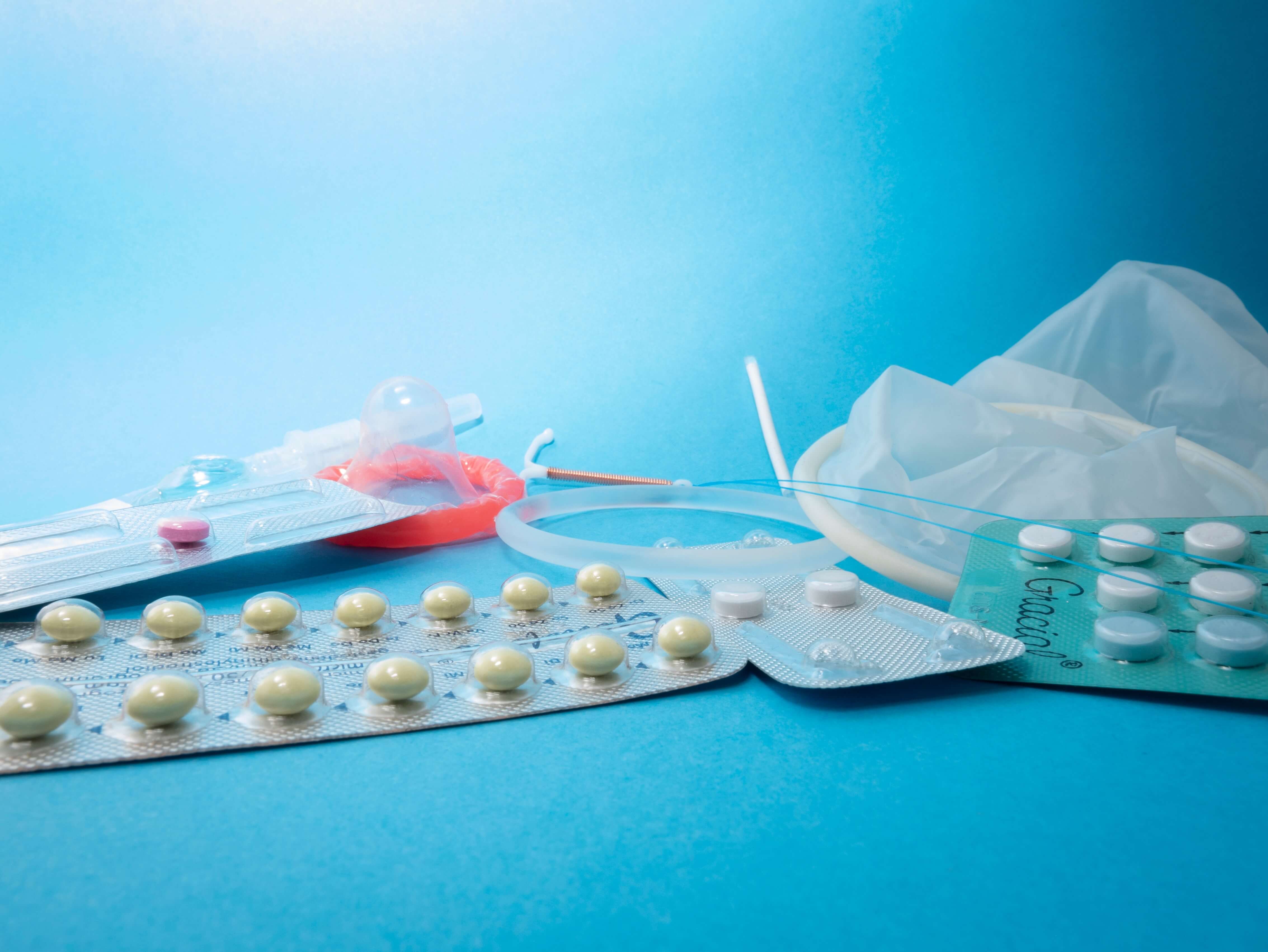 Various contraceptives on blue background, including pills and condoms, promoting safe sexual health.