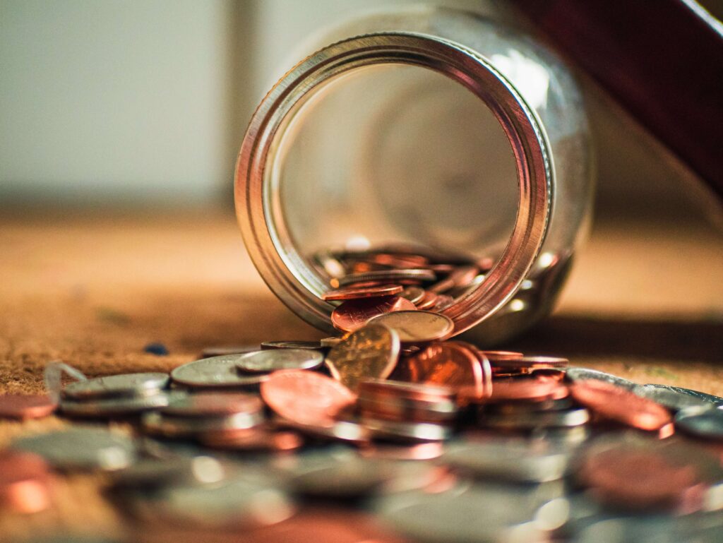 Spilled jar of mixed coins on a table, symbolising savings and financial planning in UK currency.