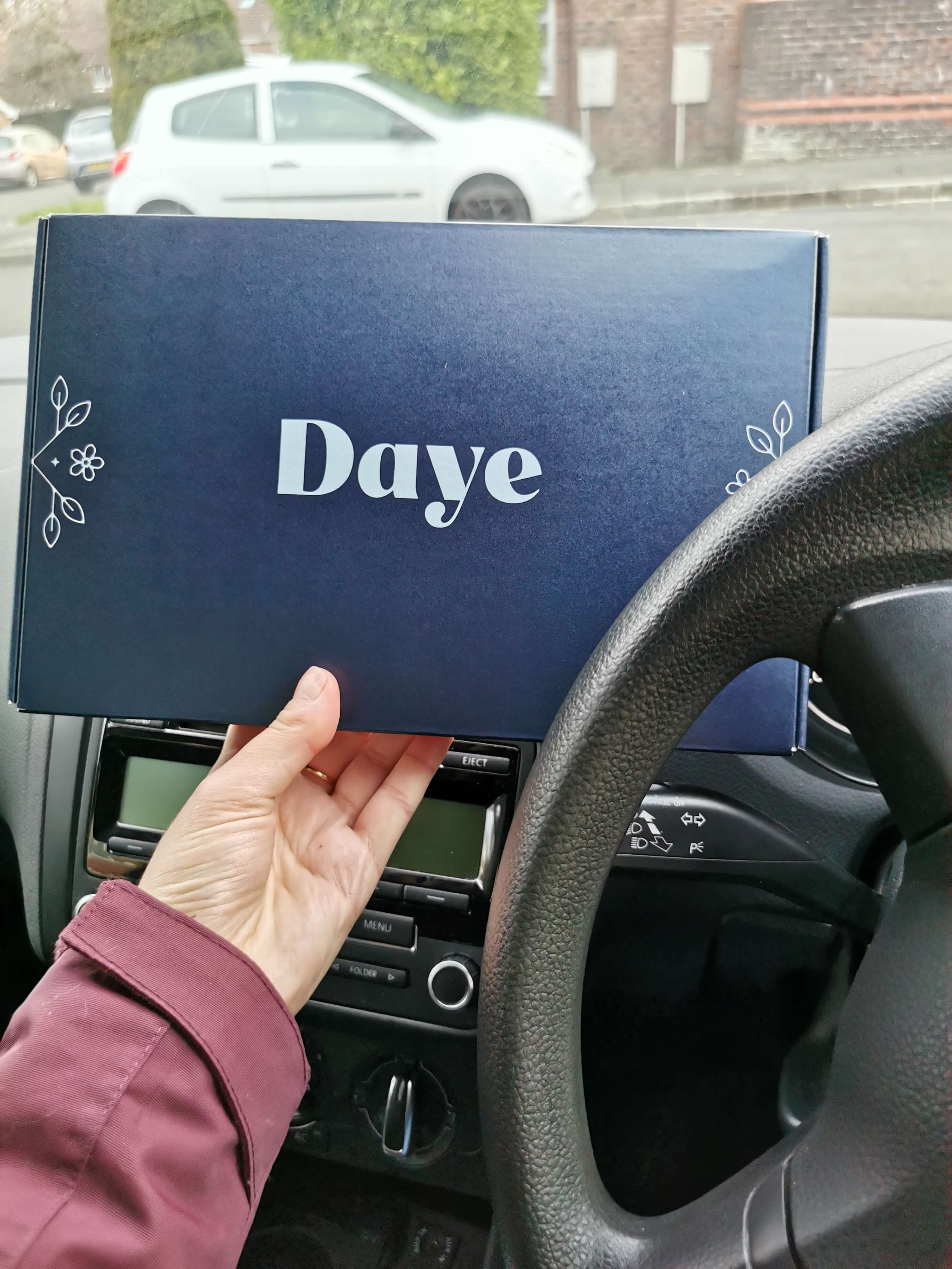 Hand holding Daye box inside car, showcasing packaging design and brand logo in a driving setting.