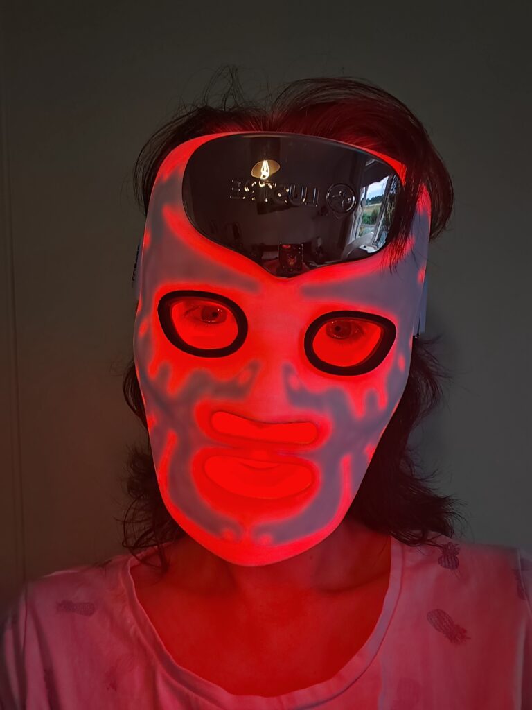 Person wearing illuminated red LED mask for skincare therapy.