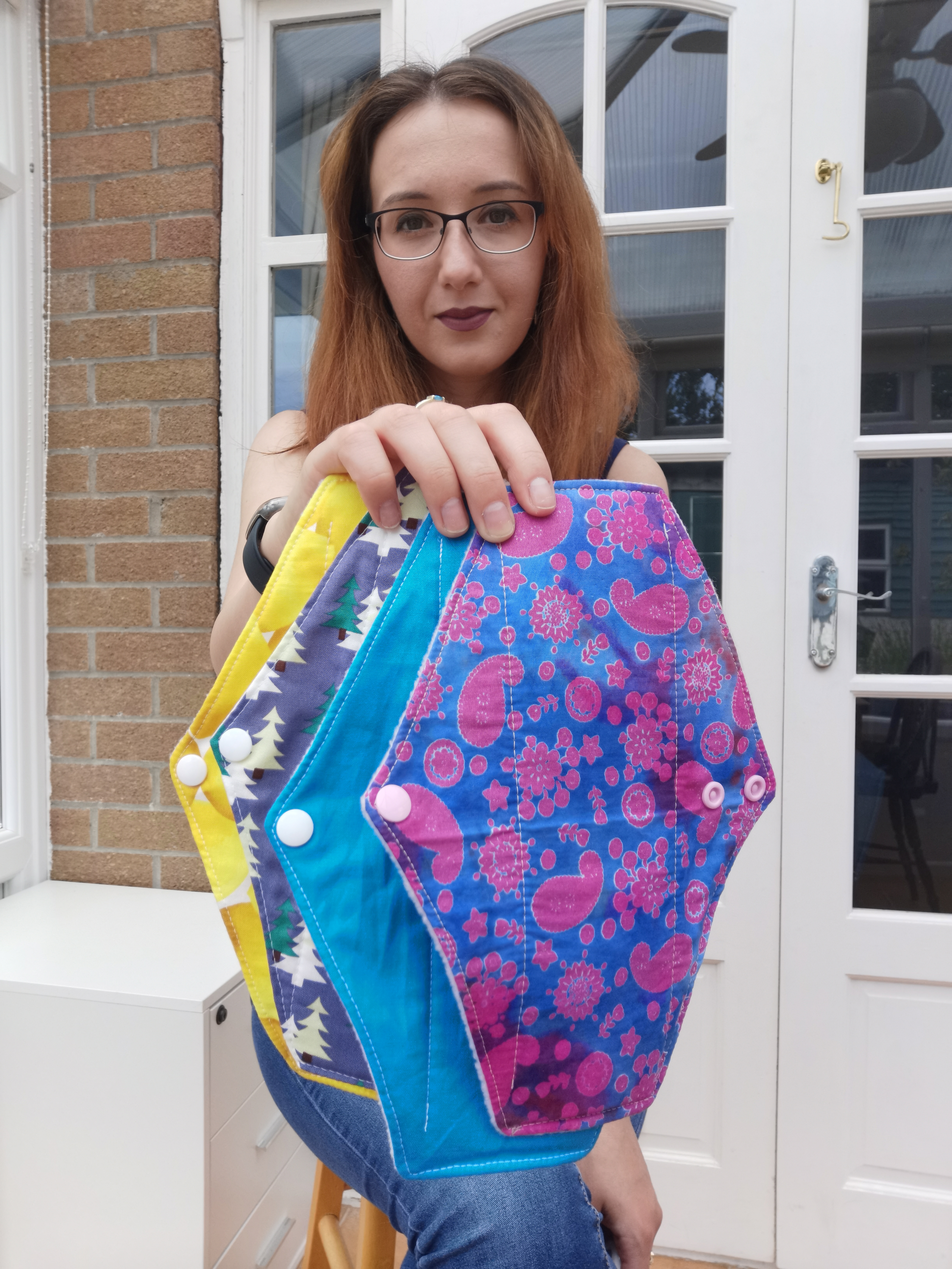 Woman holding colourful reusable cloth sanitary pads indoors.