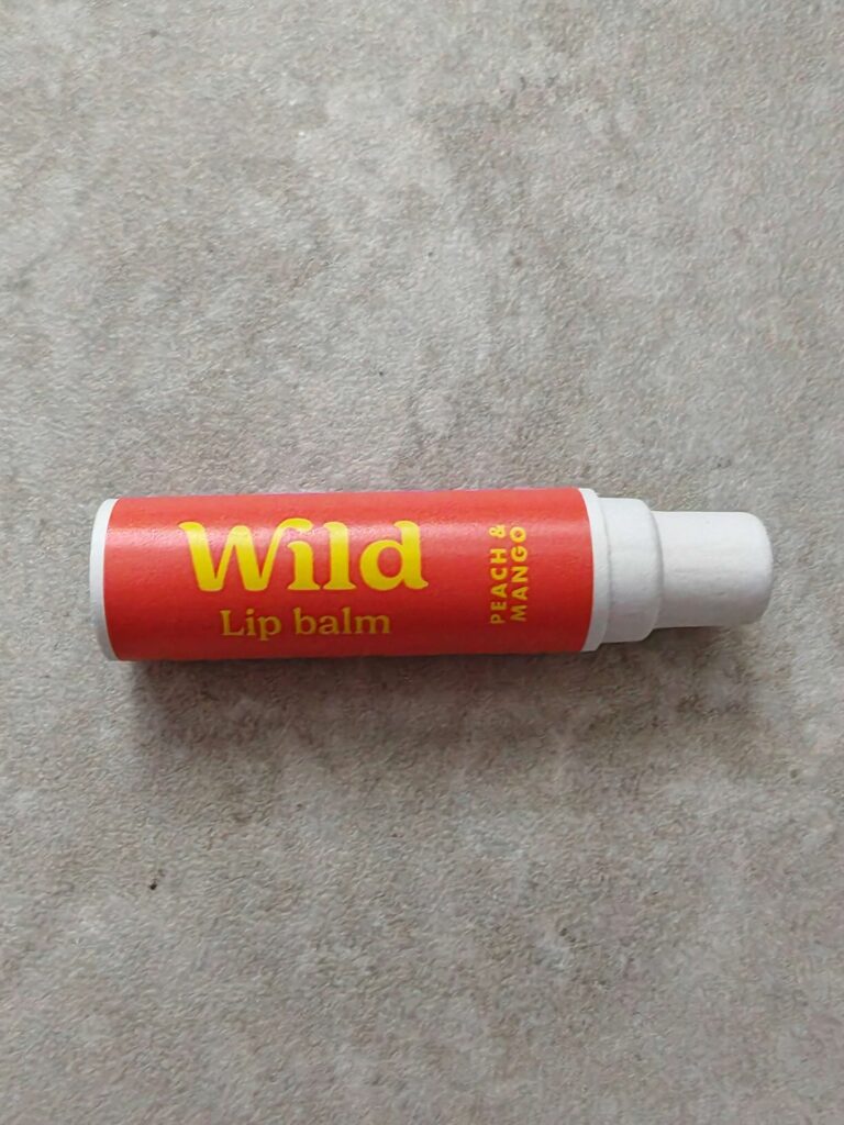 Wild lip balm in peach and mango flavour, shown on a textured grey surface, vibrant packaging.