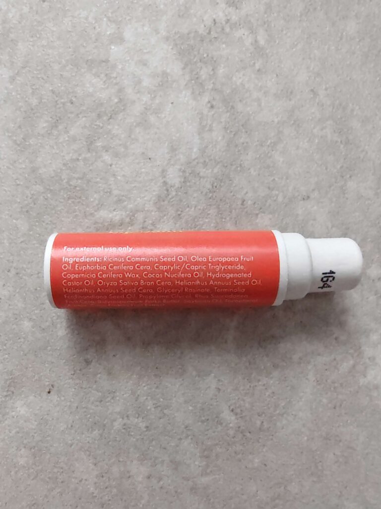Close-up of a orange tube of skincare product with ingredient list visible on a grey stone background.