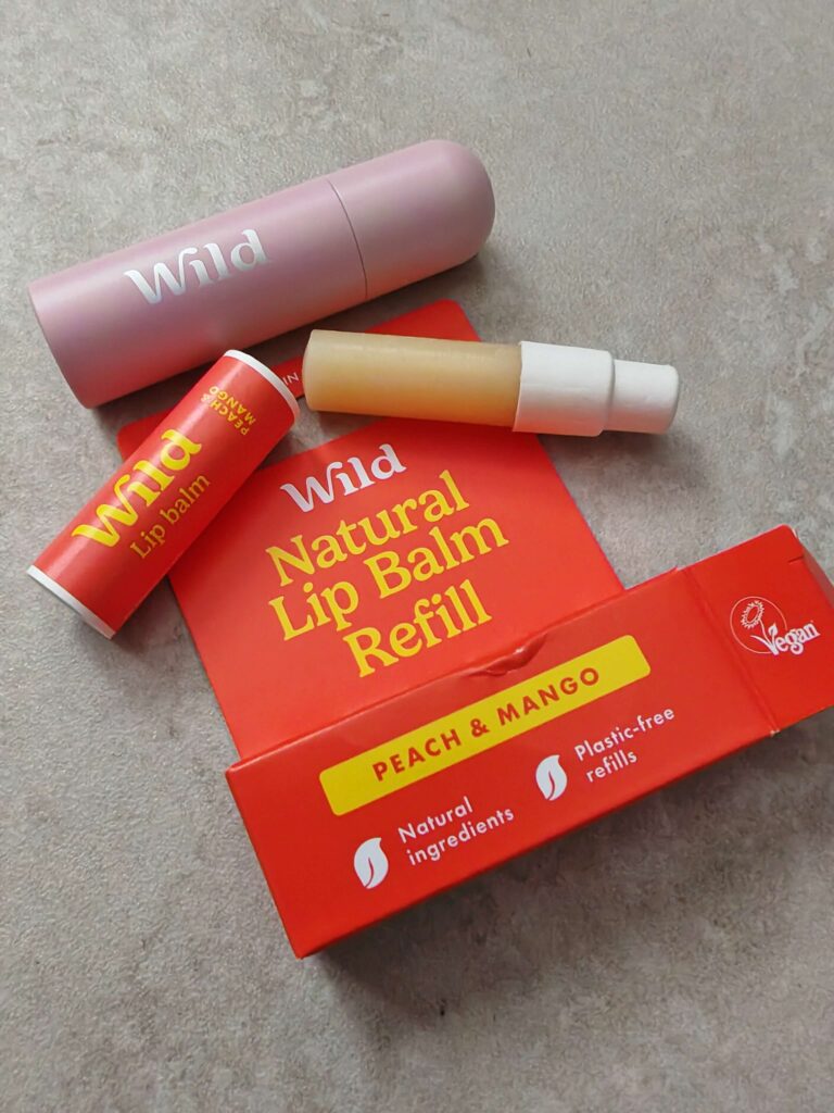 Wild natural lip balm refill in peach and mango, featuring sustainable, vegan, plastic-free packaging on a grey surface.