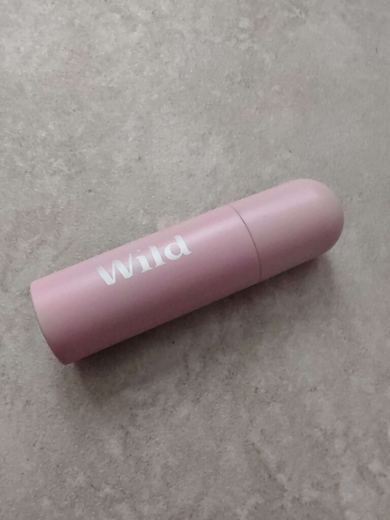 Eco-friendly pink deodorant in reusable tube on a stone surface.
