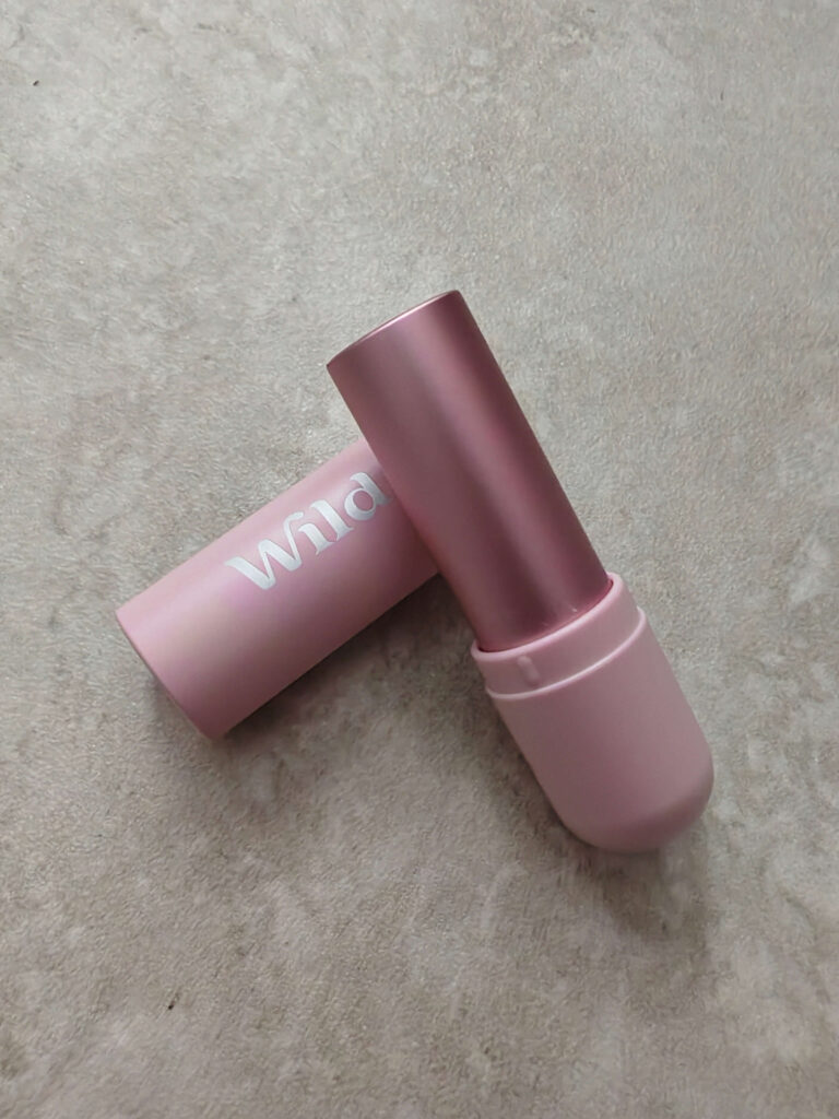 Pink Wild deodorant container on beige carpet, showcasing eco-friendly personal care product design.
