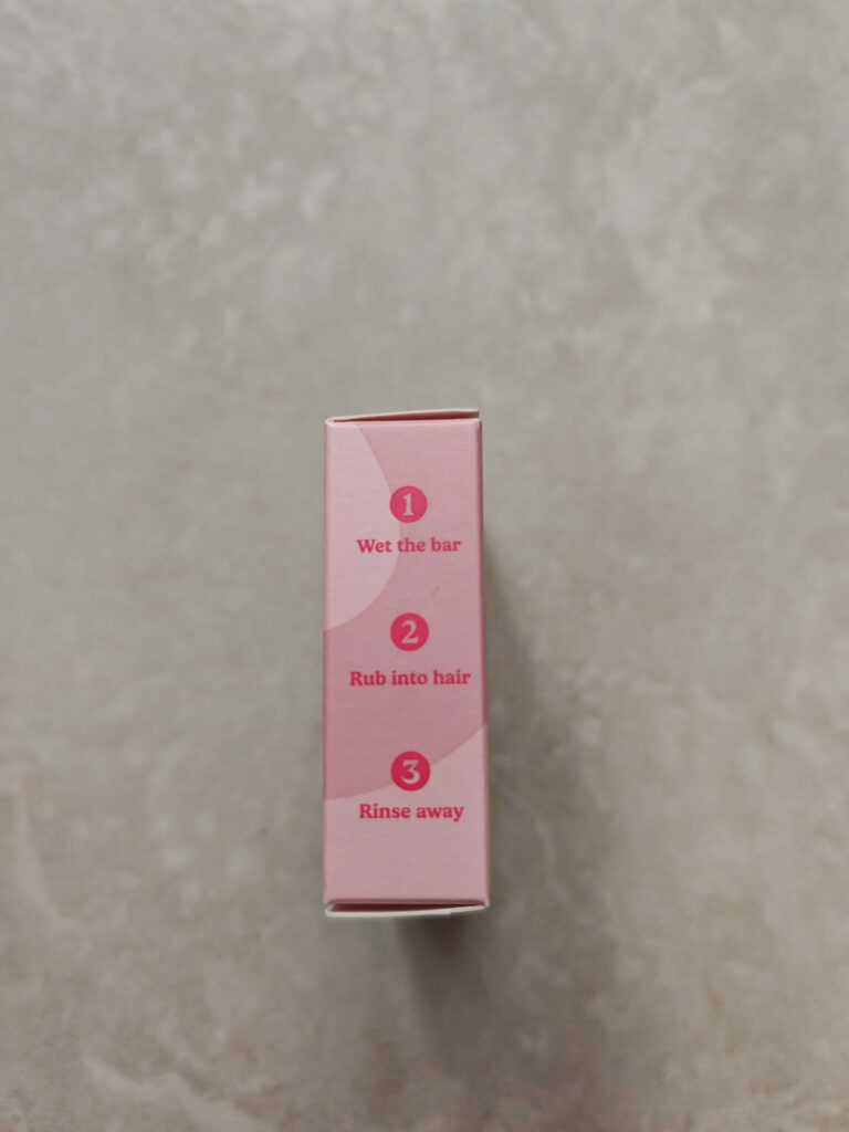 Shampoo bar instructions on pink packaging: wet the bar, rub into hair, rinse away. Simple hair care steps.