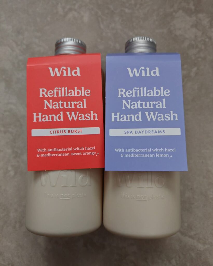 Two bottles of Wild refillable natural hand wash in Citrus Burst and Spa Daydreams scents on a grey surface.