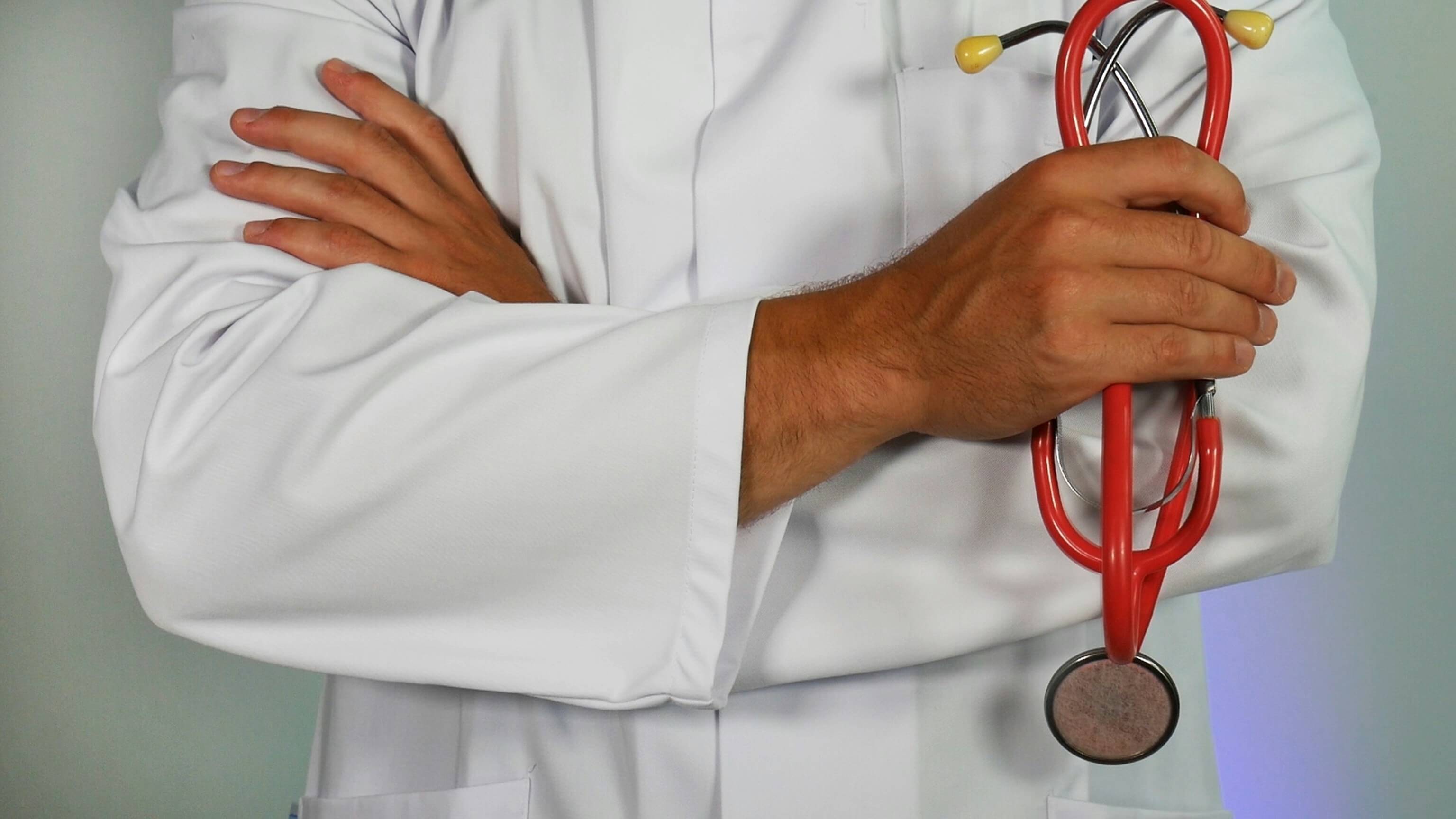 Close-up of a doctor in a white coat holding a red stethoscope, symbolising healthcare and medical professionalism.