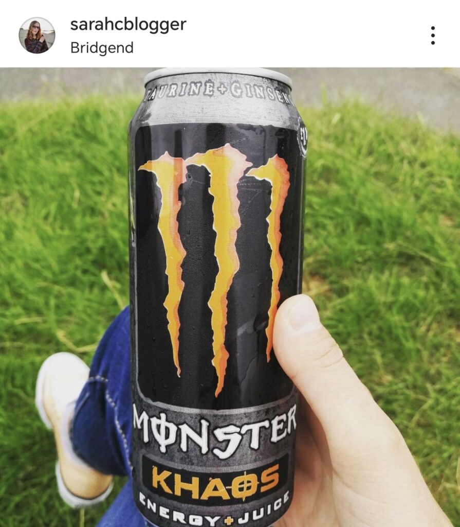 Person holding a can of Monster Khaos energy drink outdoors on grass, highlighting the bold orange logo.