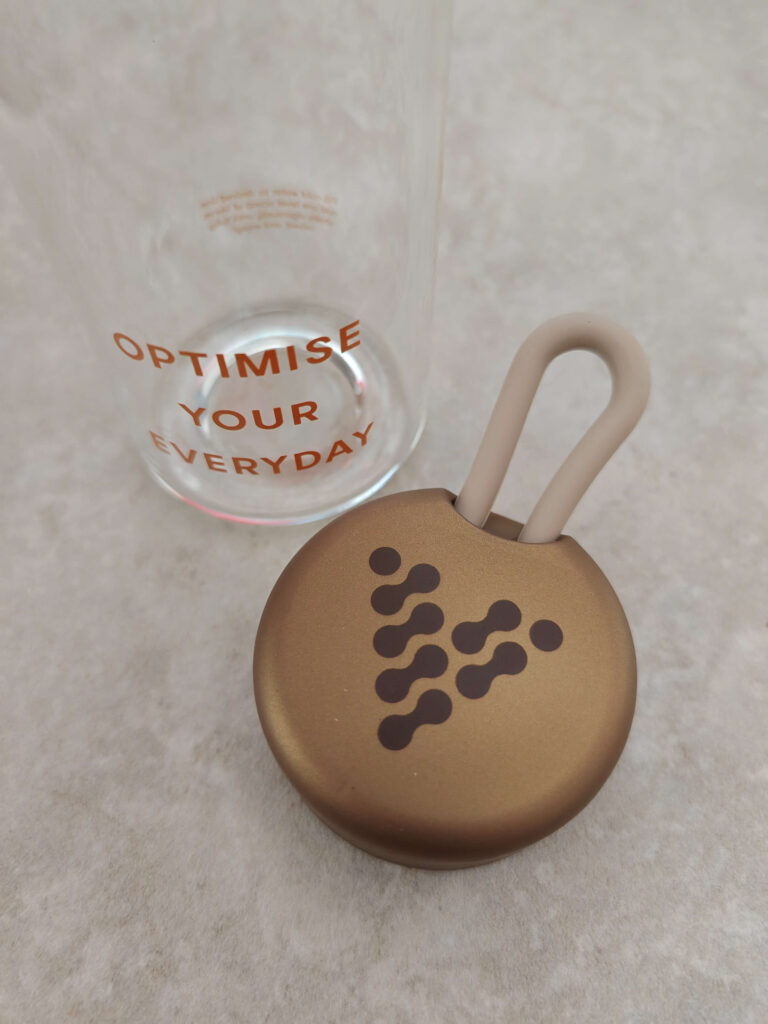 Copper puck-shaped lid with a loop next to a clear glass showing Optimise Your Everyday text.