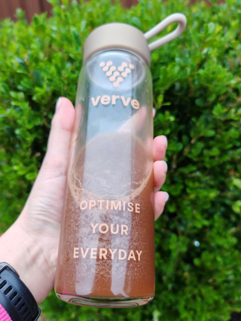 Hand holding a Verve bottle with the text OPTIMISE YOUR EVERYDAY, set against a lush green background.
