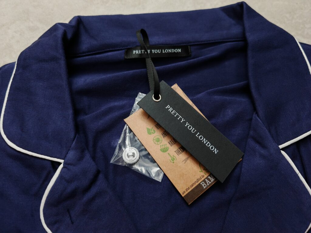 Navy blue Pretty You London pajamas with white piping and eco-friendly tags on a soft surface.
