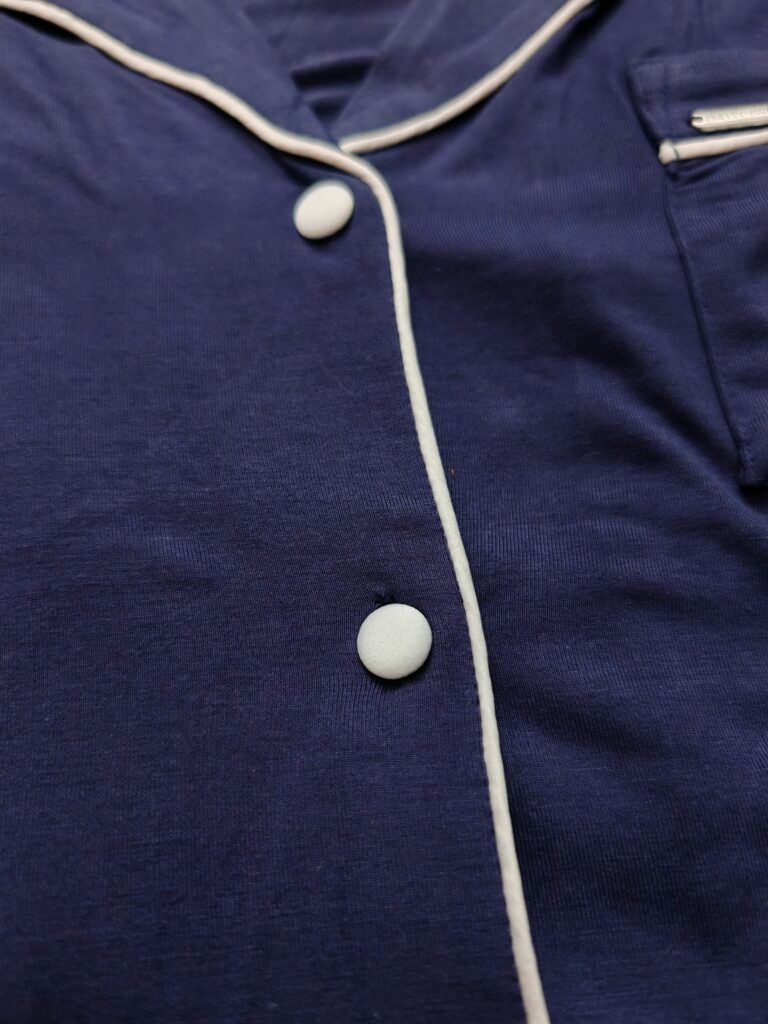Close-up of a blue pajama shirt with white piping and buttons, showcasing classic sleepwear design.