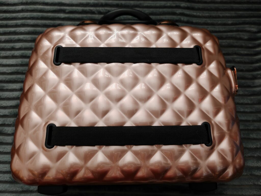 Rose gold quilted suitcase with black handles on a textured surface. Stylish, modern travel accessory.