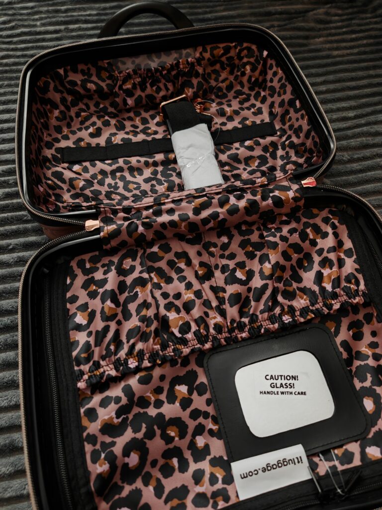 Open suitcase with leopard print lining and a Caution! Glass! label inside.
