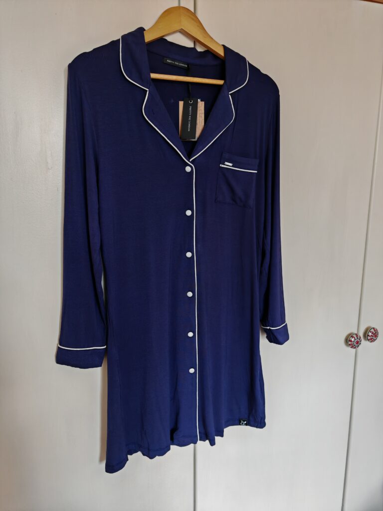 Navy blue button-up nightshirt with white piping, hanging on a wooden hanger against a white background.