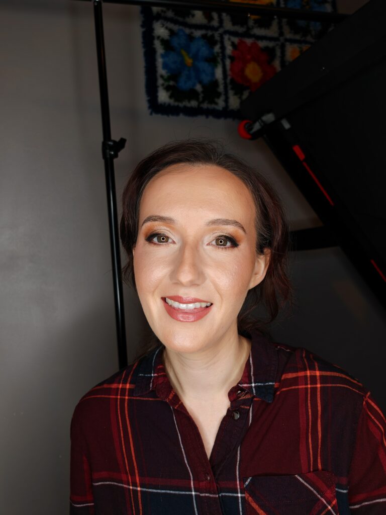 Portrait of a smiling person wearing a plaid shirt, posing in a well-lit studio setting with a floral art piece in the background.