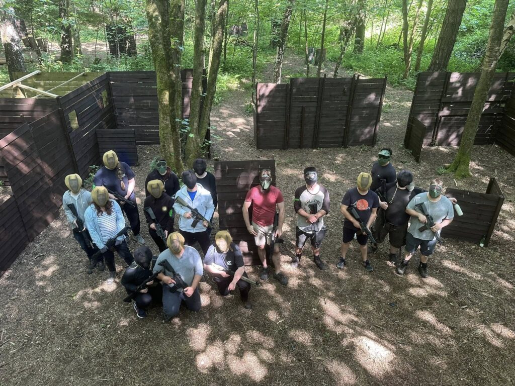 Group playing airsoft in a wooded arena with protective gear and markers, enjoying an outdoor adventure activity.
