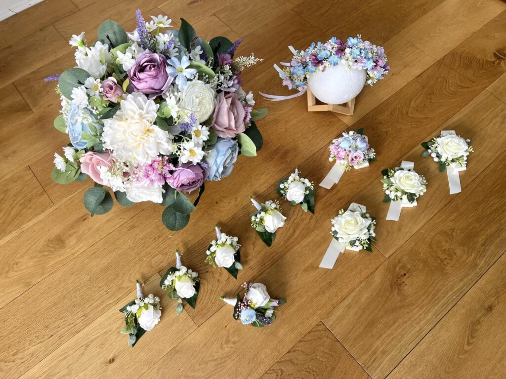 Elegant wedding flower arrangements with mixed pastel bouquets and white boutonnières on a wooden floor.