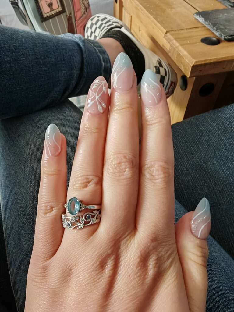 Close-up of a hand with elegant blue nail art and intricate silver rings, against a casual background.