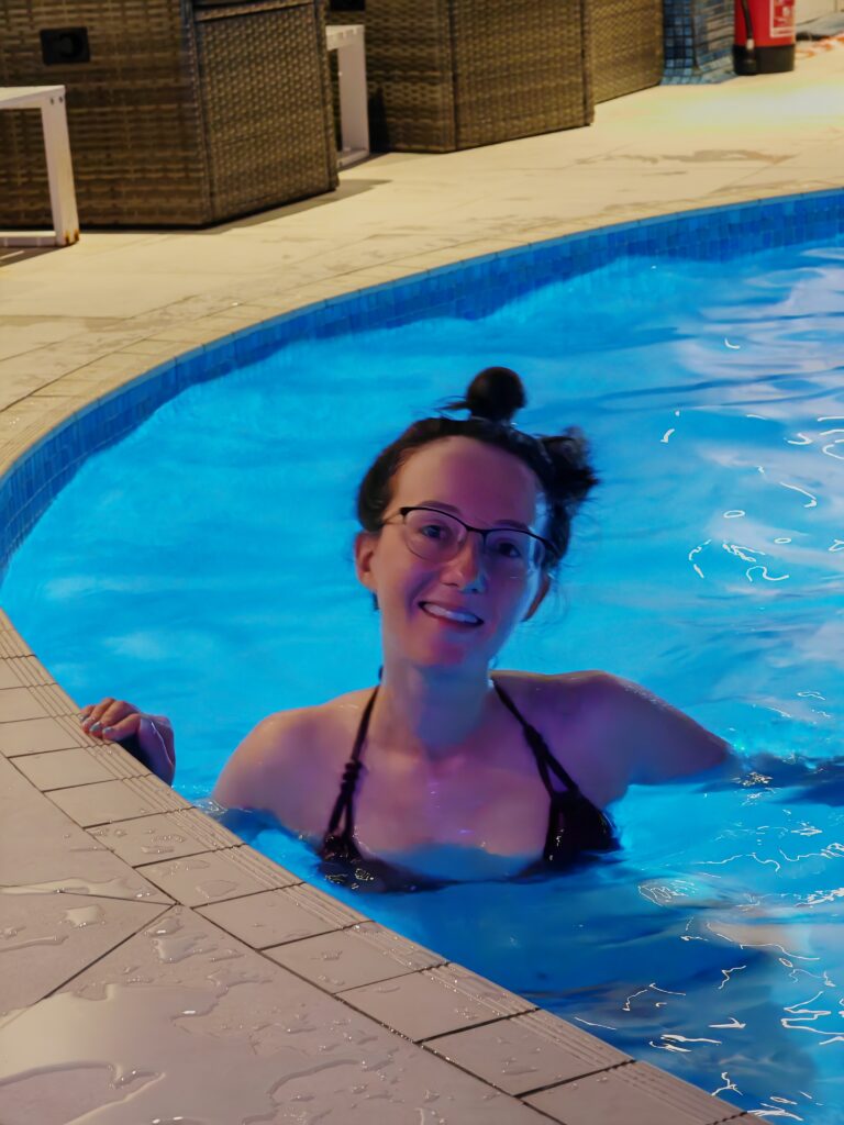 Woman smiling in a swimming pool at night, enjoying a refreshing swim under bright blue pool lights.