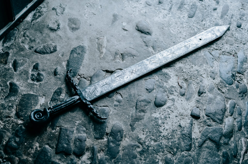 Ancient sword with runes on a stone floor, symbolizing Pagan history and craftsmanship.