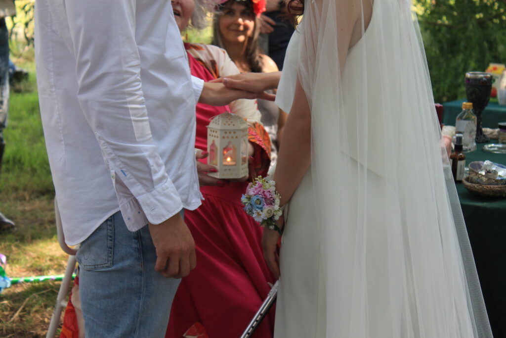 Wedding ceremony outdoors with couple holding hands, surrounded by guests and a decorative candle lantern.