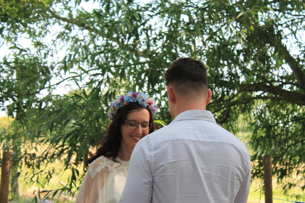 Bride and groom exchange vows under a canopy of lush trees during an outdoor wedding ceremony.
