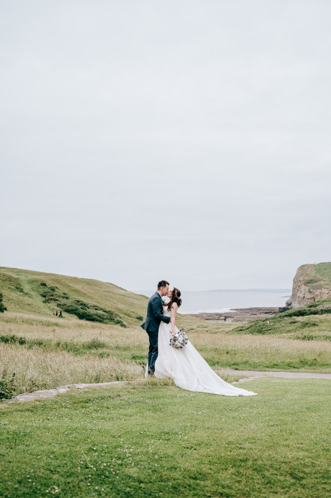 Bride and groom share a kiss in scenic outdoor wedding with ocean view.