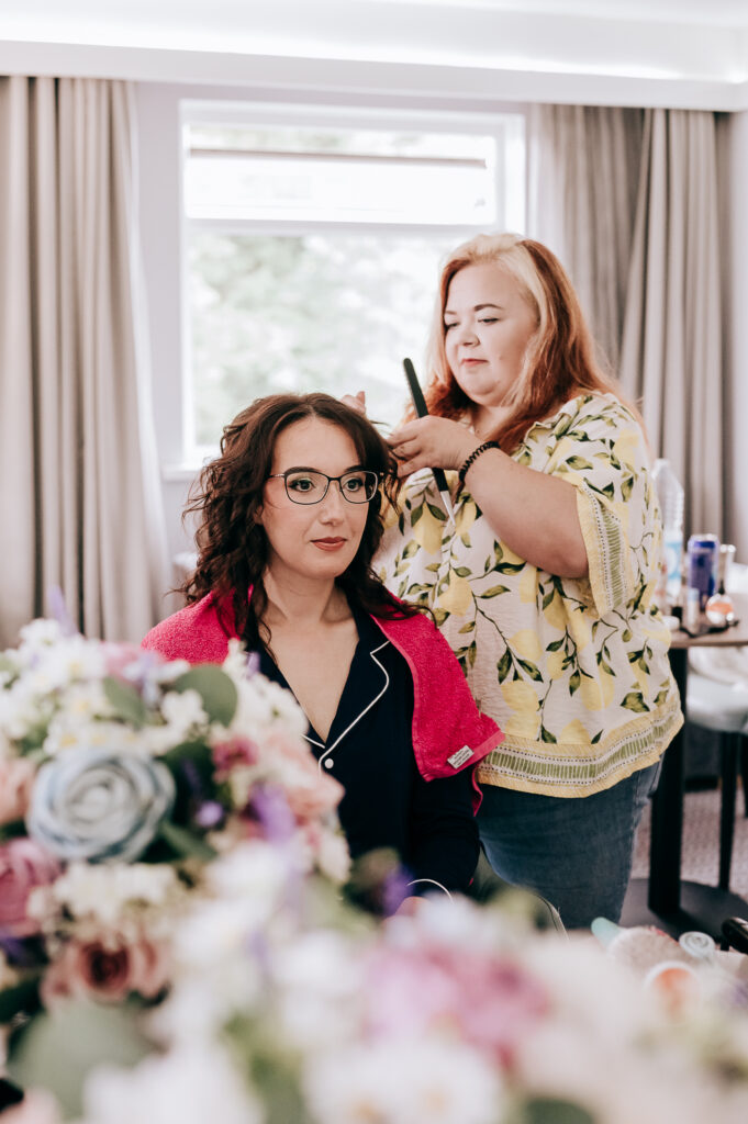 Woman having hair styled in salon, surrounded by colorful flowers.