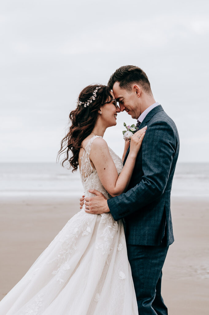 Bride and groom embrace lovingly on a beach, showing their wedding attire and romantic connection.