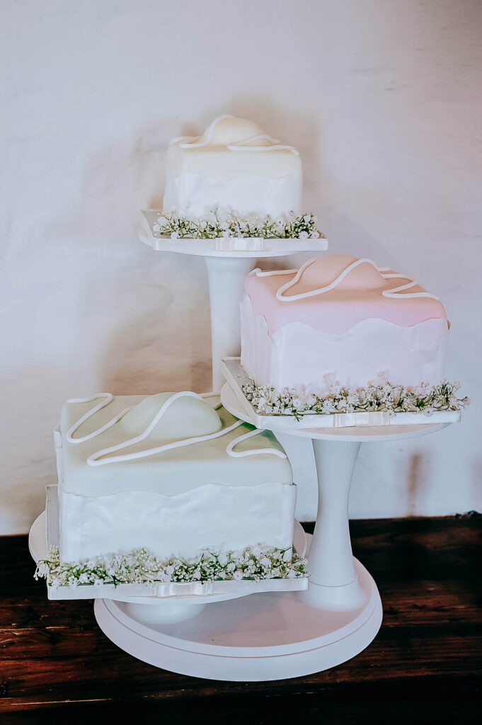 Three-tier pastel wedding cakes with white piping and floral accents on white stands.
