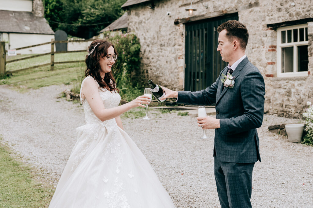 Bride and groom celebrate with champagne toast outside rustic stone building.