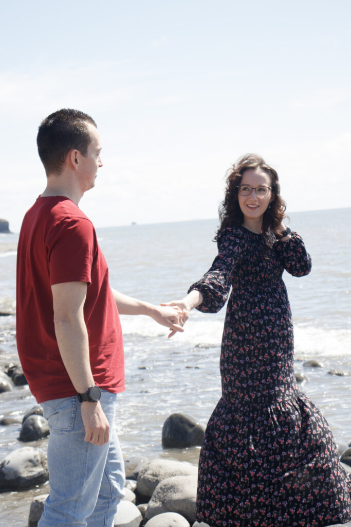 Couple holding hands by the ocean, enjoying a sunny day on a rocky beach. Romantic and carefree moment.