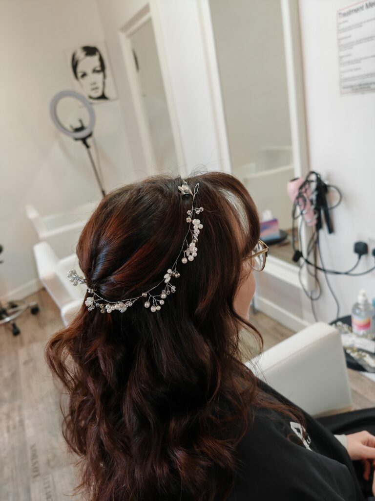 Brunette woman with pearl hair accessory in a salon, sitting with curled hairstyle near a vanity.