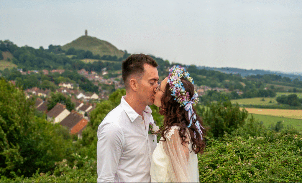 Romantic couple kissing at a scenic viewpoint with lush hills in the background.