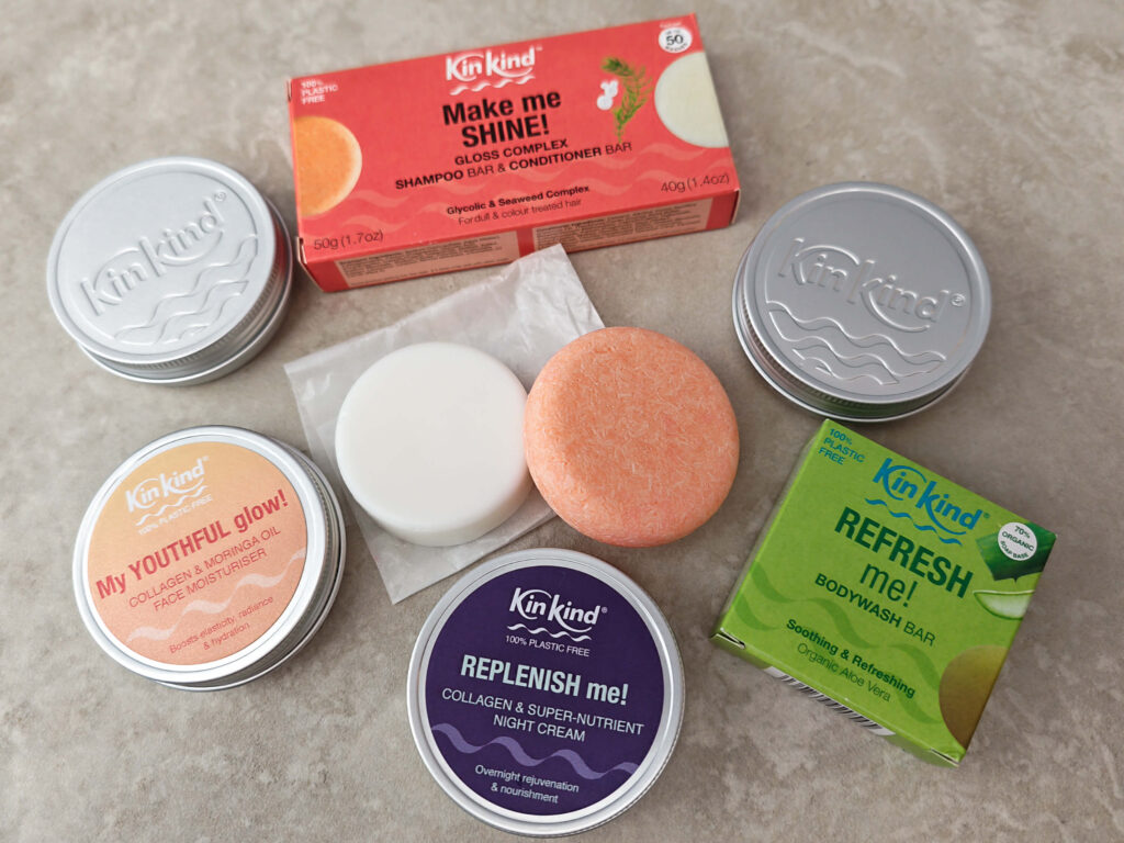 Plastic-free KinKind skincare and haircare bars, including shampoo, conditioner, and moisturisers, on a grey surface.