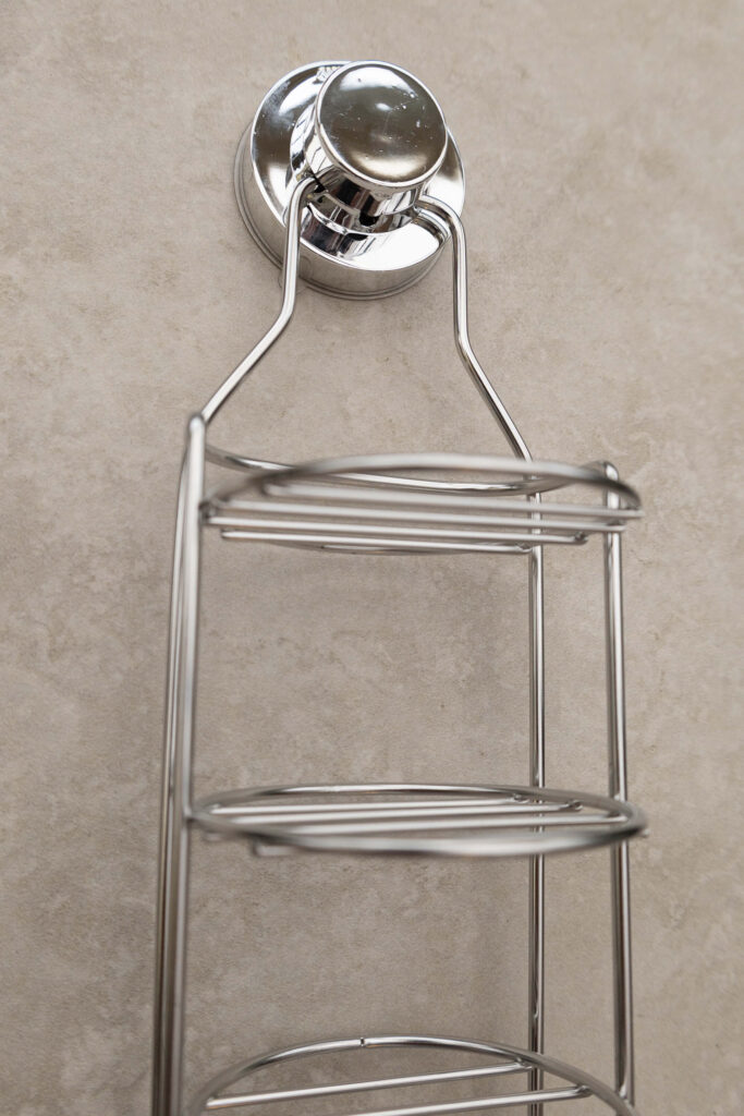 Wall-mounted chrome shower caddy with suction cup attachment on a tiled background.