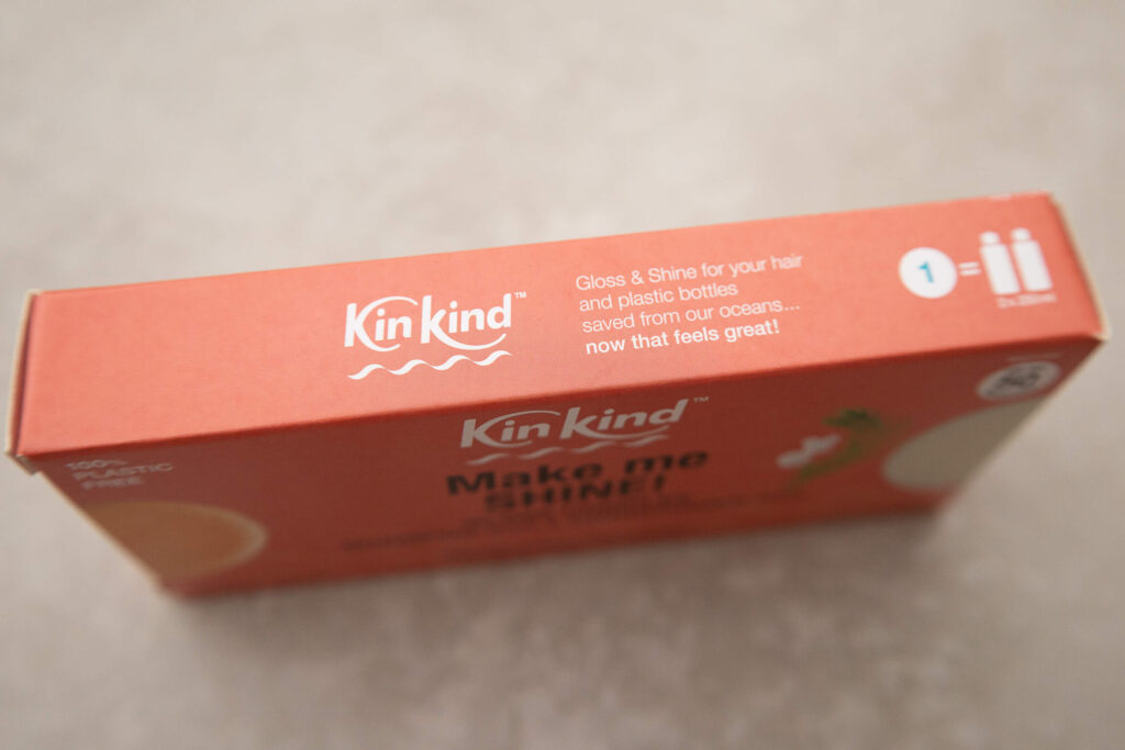 Eco-friendly KinKind shampoo bar packaging with text promoting gloss and shine while reducing ocean plastic.